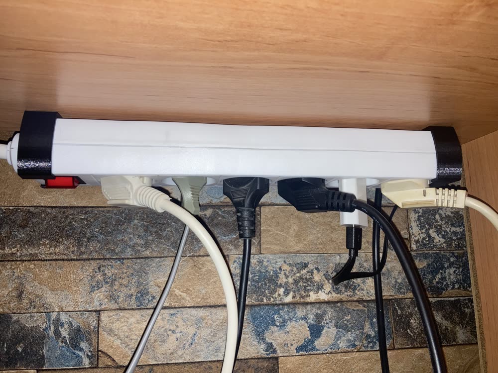 The original: two black end caps holding a white power strip under a desk.